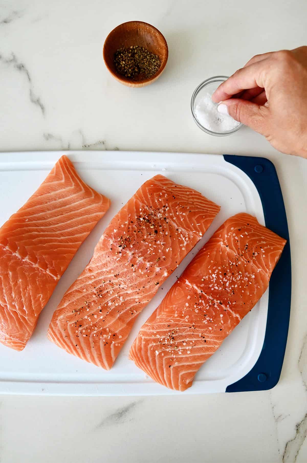 Seasoning salmon filets with salt and pepper before pan-searing.