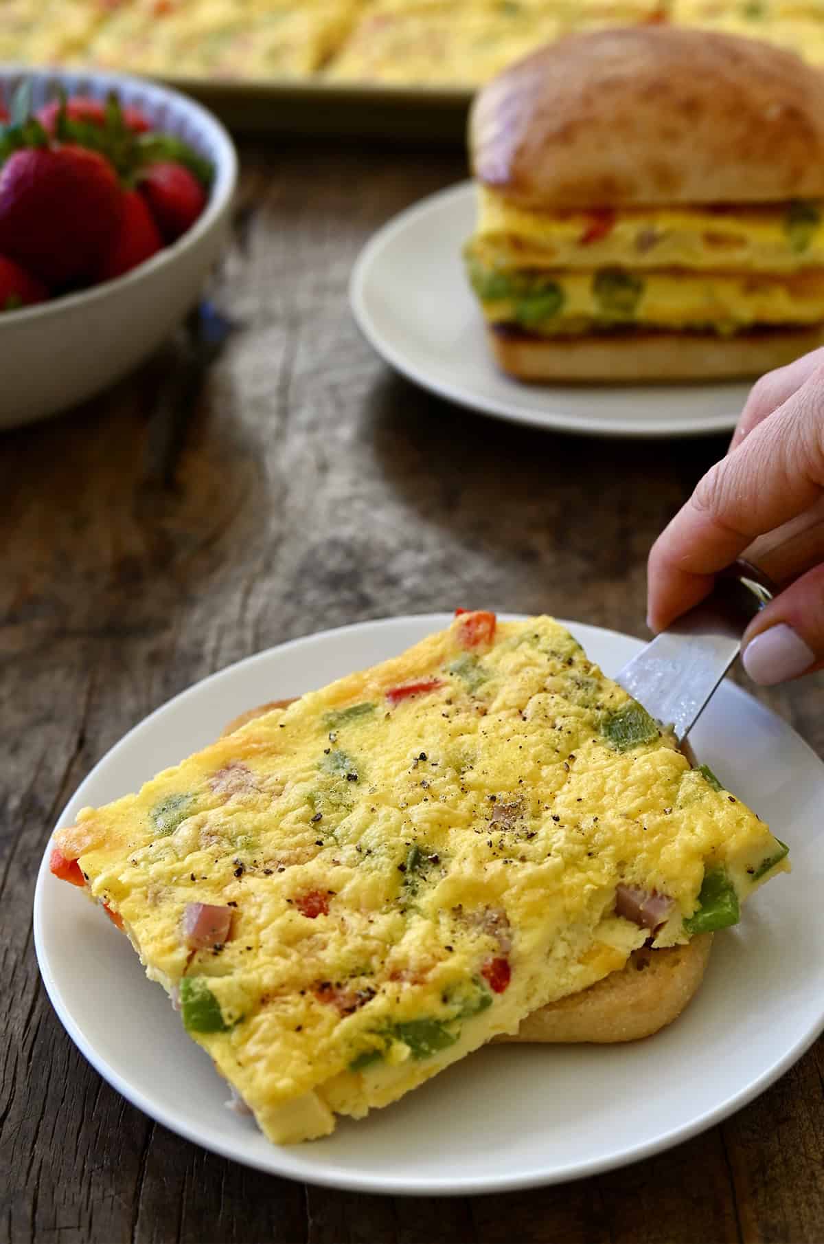 A square of a sheet pan egg being served on a plate with a toasted ciabatta roll.