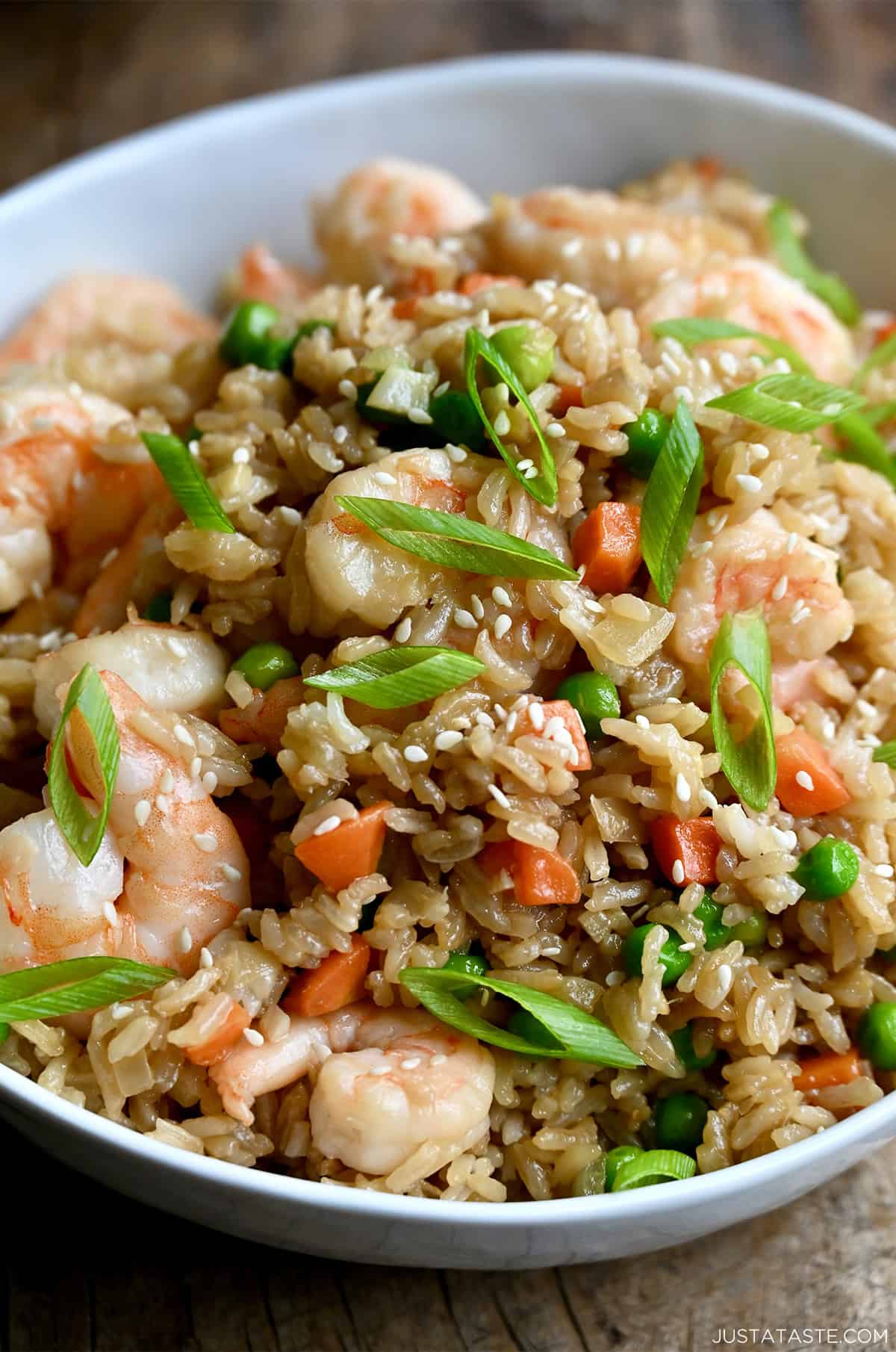 A close-up of shrimp fried rice with peas and carrots garnished with sliced scallions and sesame seeds.