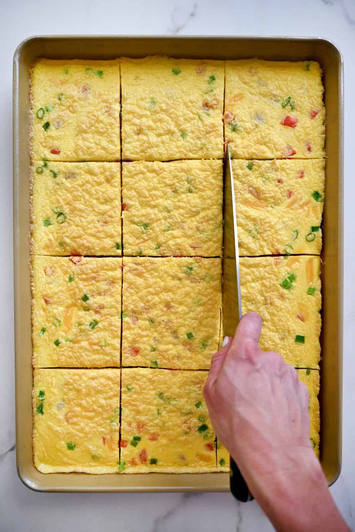 Using a sharp knife to slice sheet pan eggs into squares.