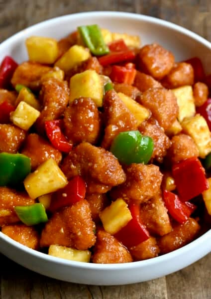 Homemade sweet and sour chicken with pineapple chunks, chopped red bell pepper and chopped green bell pepper in a bowl.