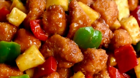 Homemade sweet and sour chicken with pineapple chunks, chopped red bell pepper and chopped green bell pepper in a bowl.