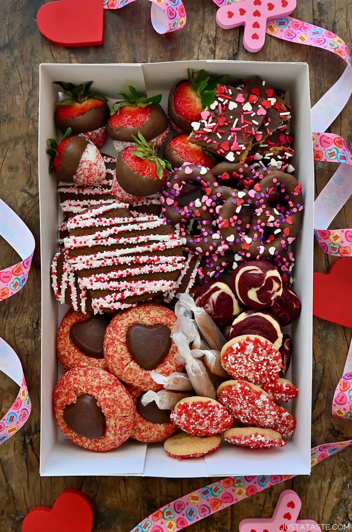 Valentine's Day dessert box with chocolate sugar cookies, white chocolate-covered strawberries, chocolate-covered pretzels, salted caramels and red velvet cheesecake brownie bites.