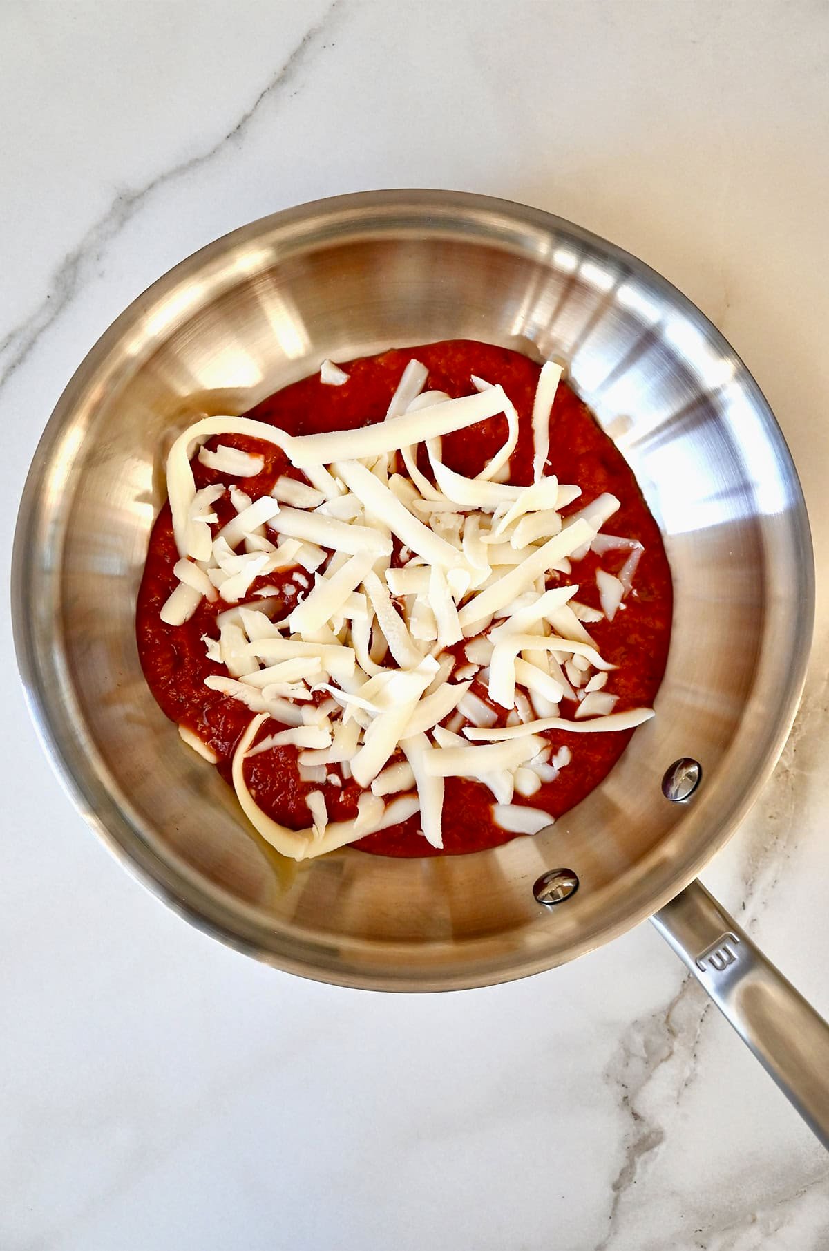 Marinara sauce topped with shredded mozzarella cheese in a skillet.