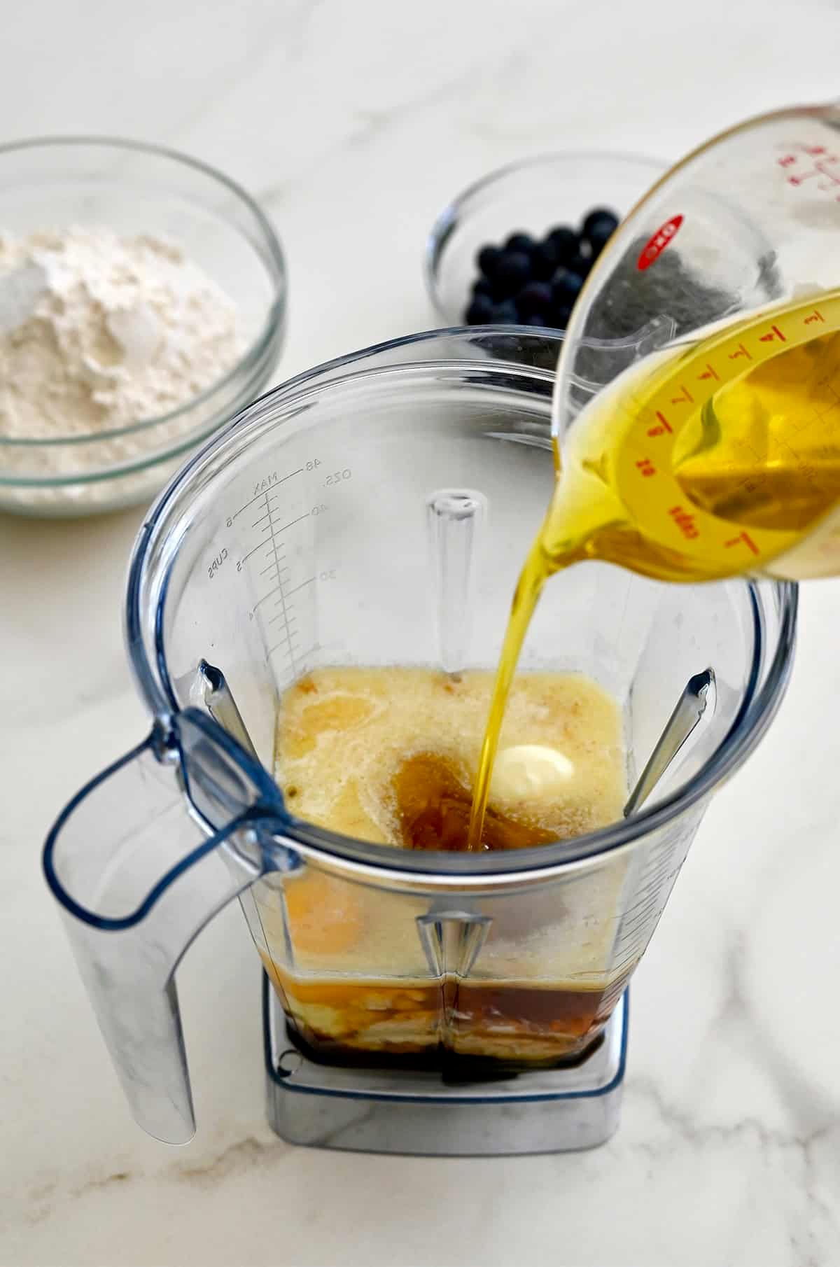 Adding olive oil to a blender with eggs, vanilla extract, honey, cottage cheese and melted butter.