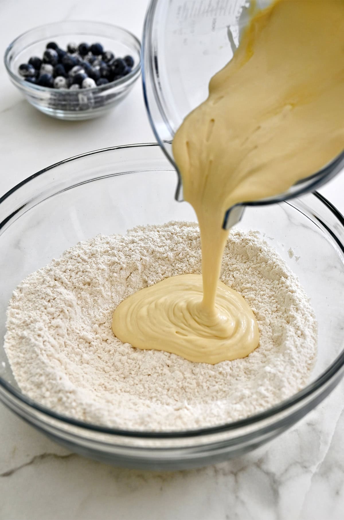 Pouring a blended cottage cheese mixture into a large bowl containing dry ingredients to make a muffin batter.