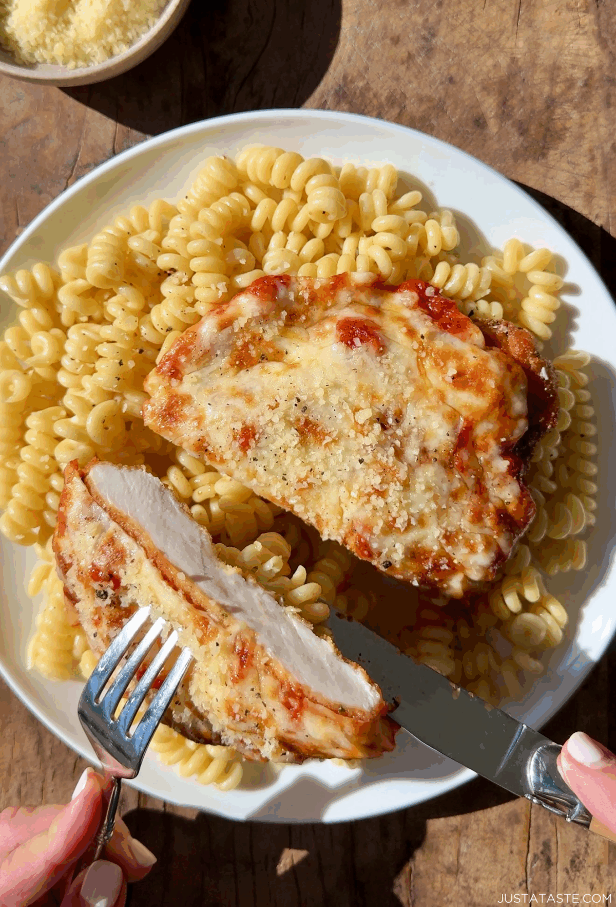 Juicy chicken parmigiana atop cacio e pepe pasta on a dinner plate.