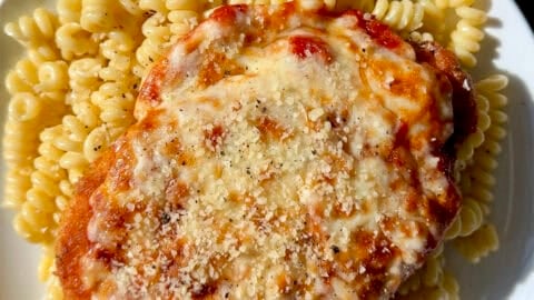 Chicken parmesan (a crispy breaded chicken cutlet topped with marinara sauce and melted mozzarella cheese) atop cacio e pepe pasta on a dinner plate.