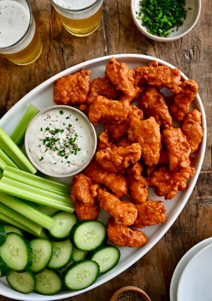 Boneless Buffalo wings on a serving platter with a small bowl containing blue cheese dressing, plus sliced cucumbers and celery.