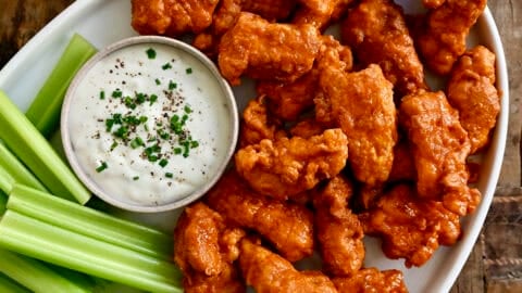 Boneless Buffalo wings on a serving platter with a small bowl containing blue cheese dressing, plus sliced cucumbers and celery.