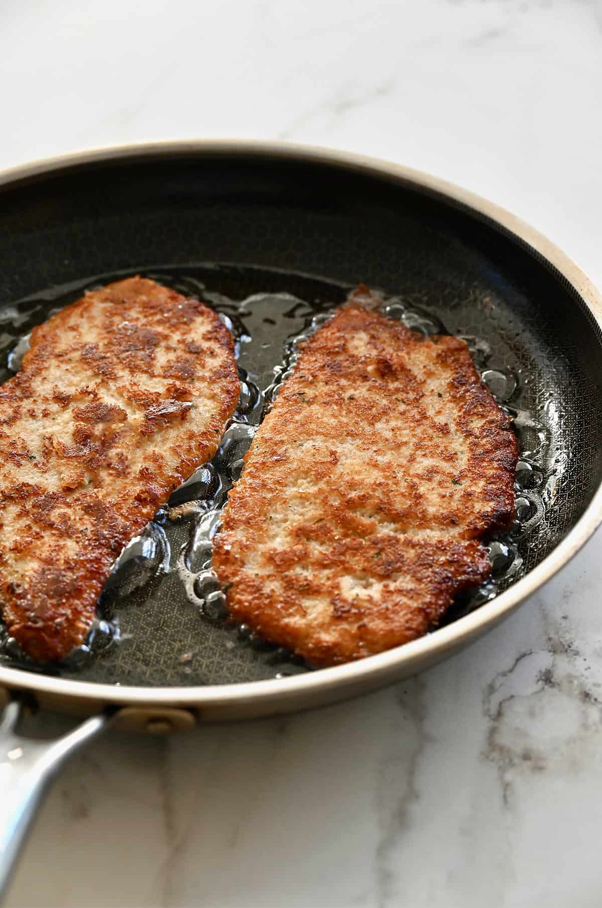Golden brown, crispy chicken cutlets in a pan.