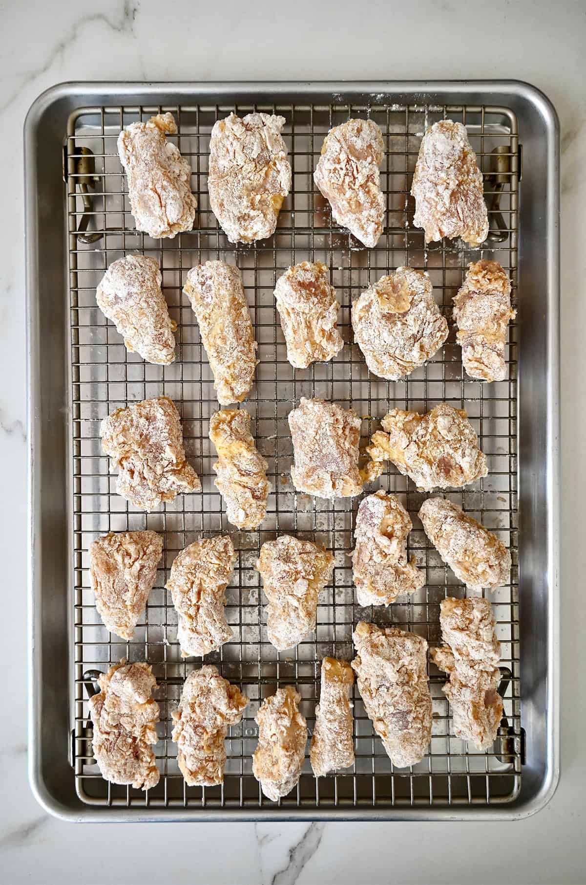 Lightly battered boneless chicken wings on a wire rack atop a baking sheet.