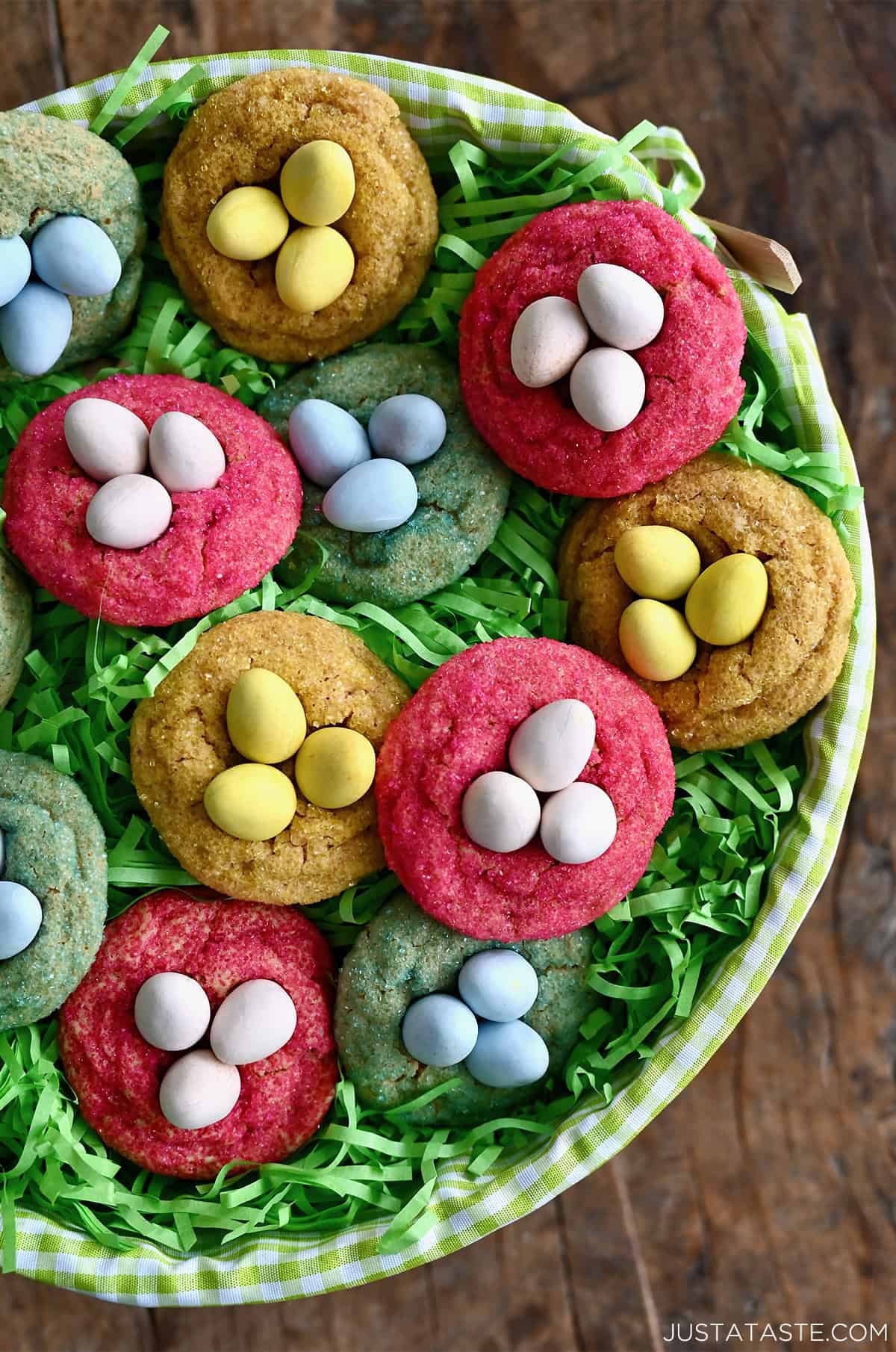 Peanut butter Cadbury Mini Egg cookies rolled in pink, blue and yellow sanding sugar, topped with crunchy Mini Cadbury Eggs nestled atop green confetti paper.