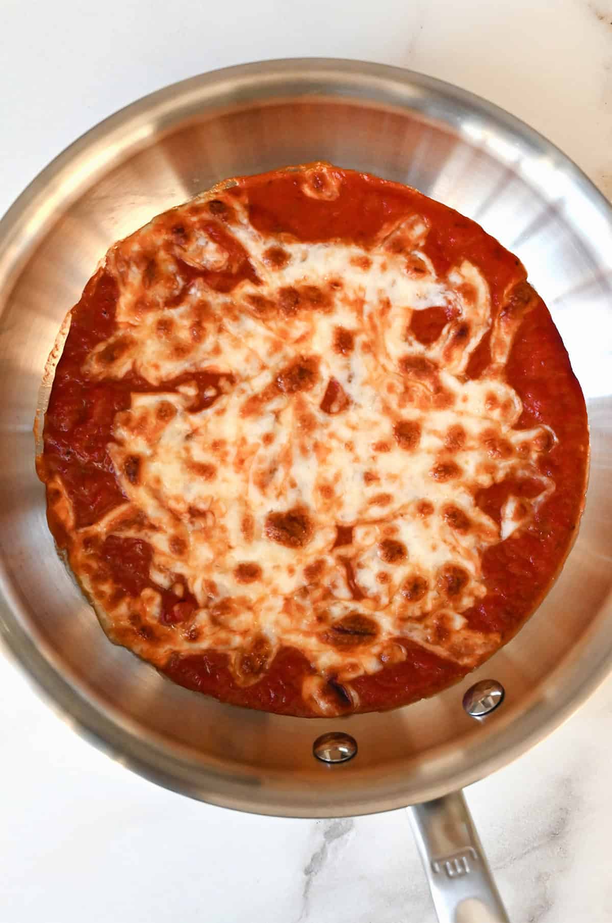 Melted mozzarella cheese atop warm marinara sauce in a skillet.