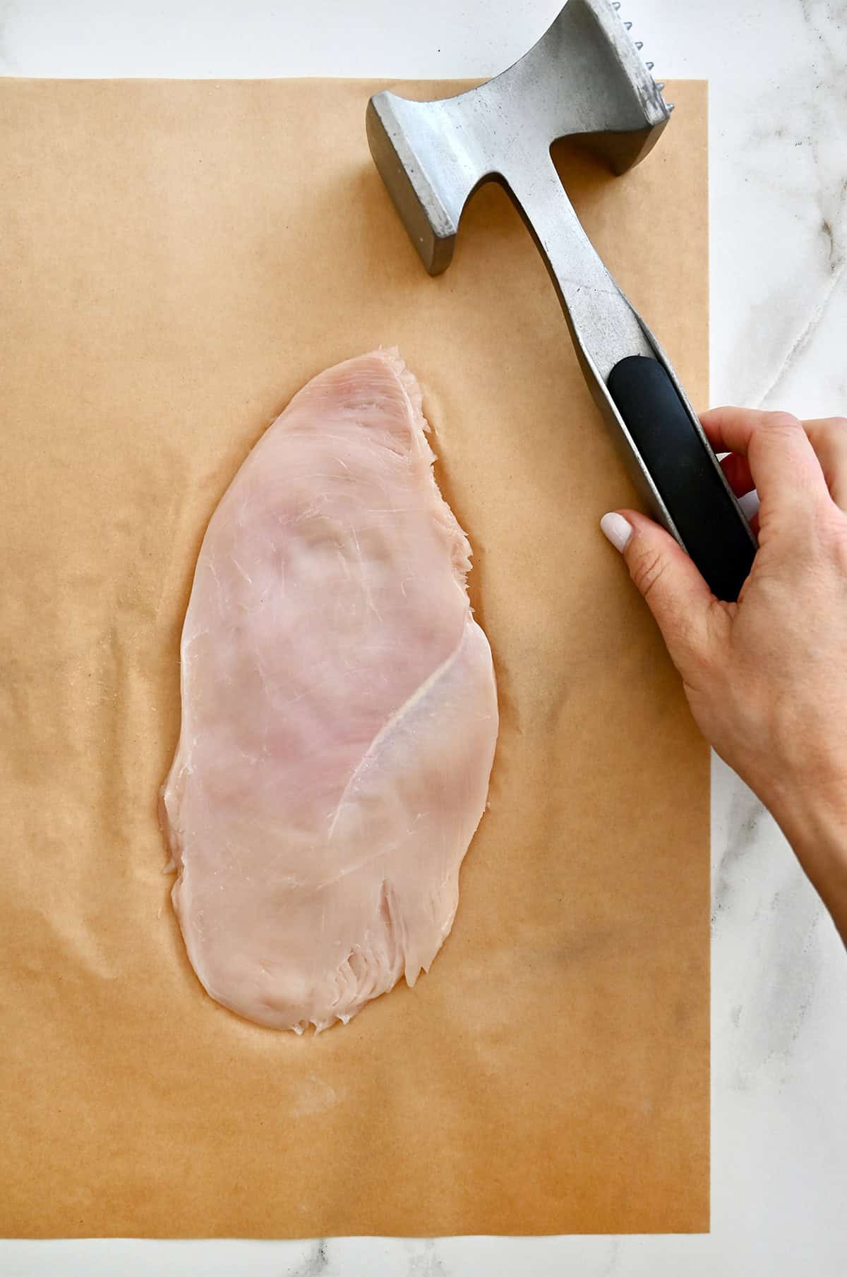 Using a meat mallet to pound a boneless, skinless chicken breast very thin.
