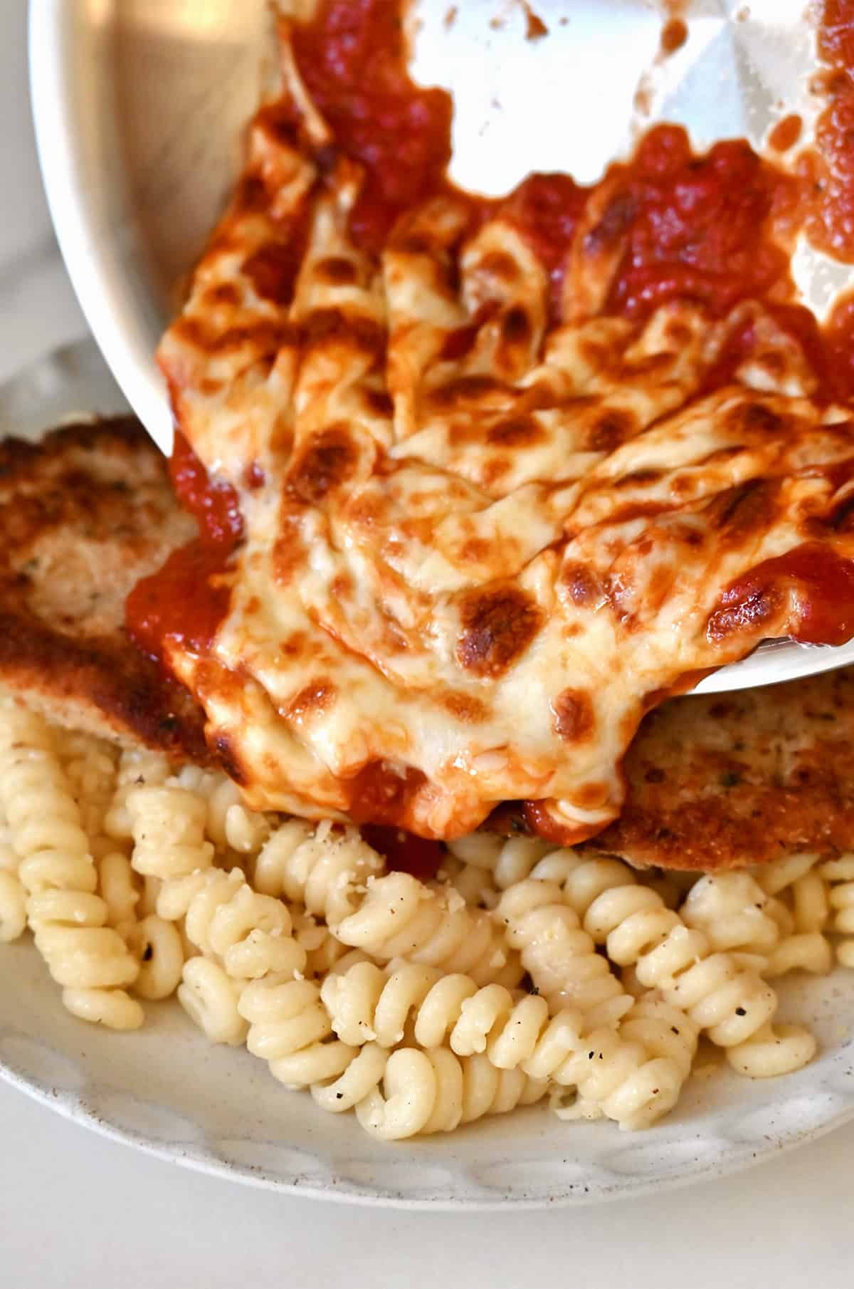Pouring marinara sauce with melted mozzarella atop crispy chicken cutlets to make the best chicken parmesan.