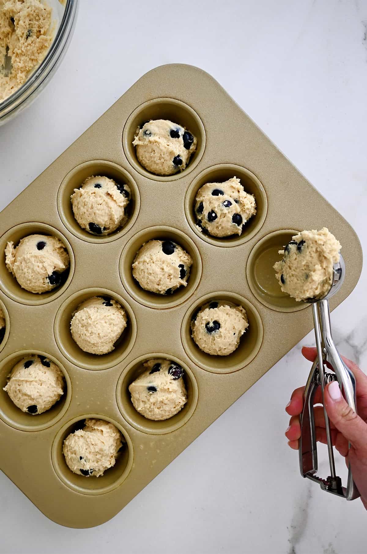Scooping blueberry cottage cheese muffin batter into a standard-size muffin pan.