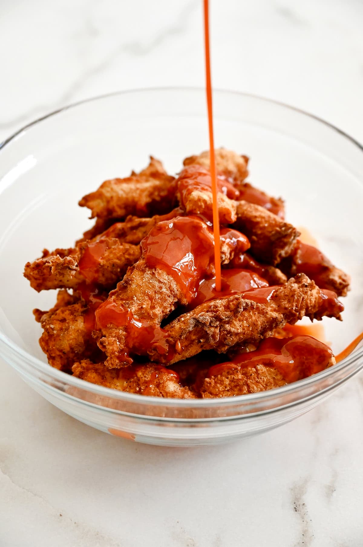 Boneless chicken wings being tossed in Buffalo sauce.