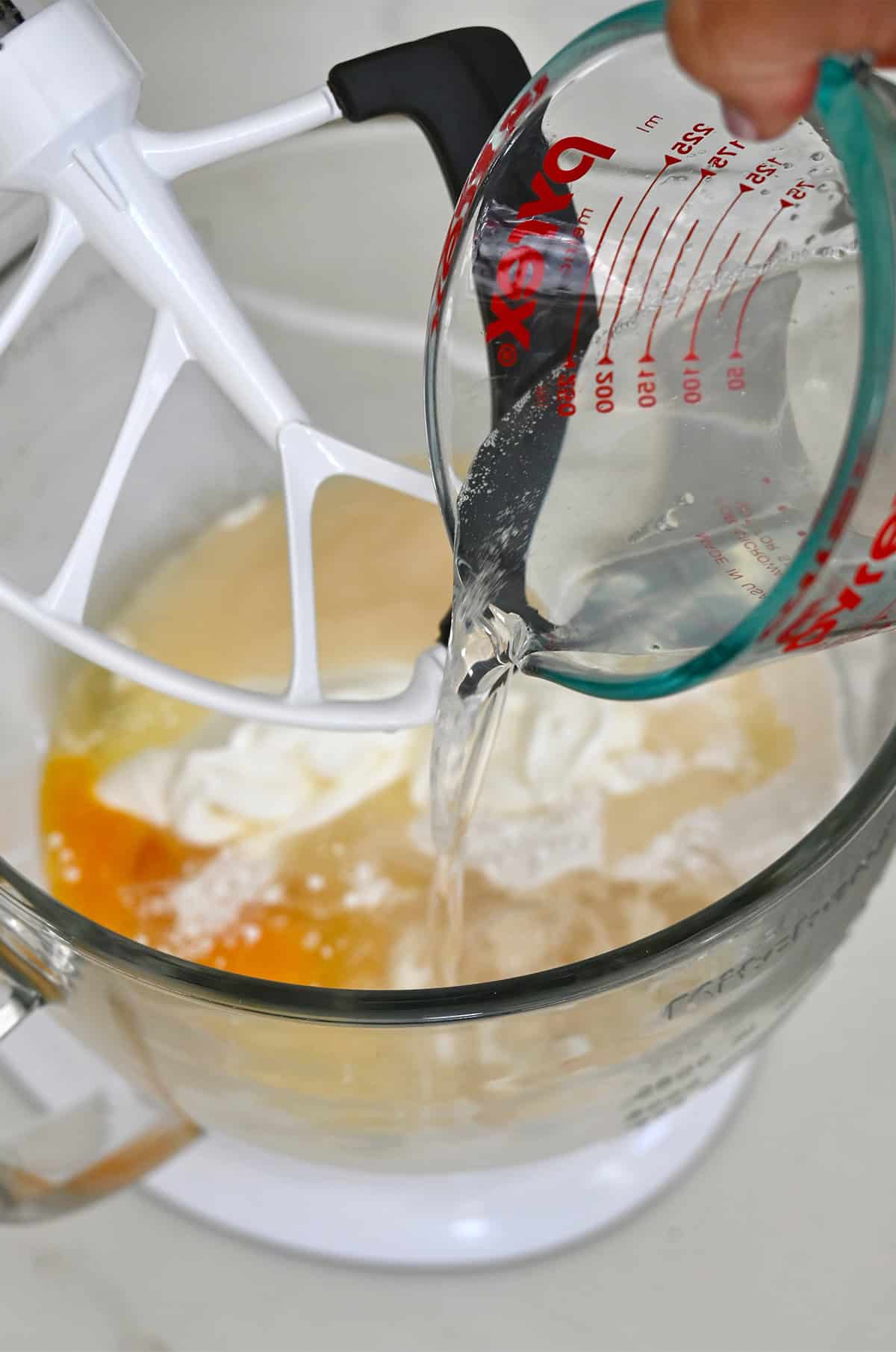 Adding melted coconut oil to a bowl with coconut cream, eggs, vanilla extract, melted butter and white cake mix.