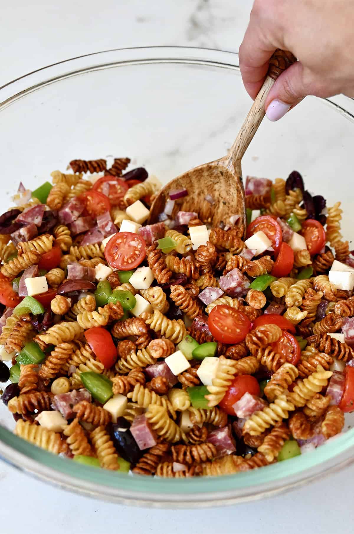 Tossing crispy noodles, along with fresh veggies, provolone cheese and cubes of hard salami in a homemade red wine vinaigrette in a large glass bowl with a wooden spoon.