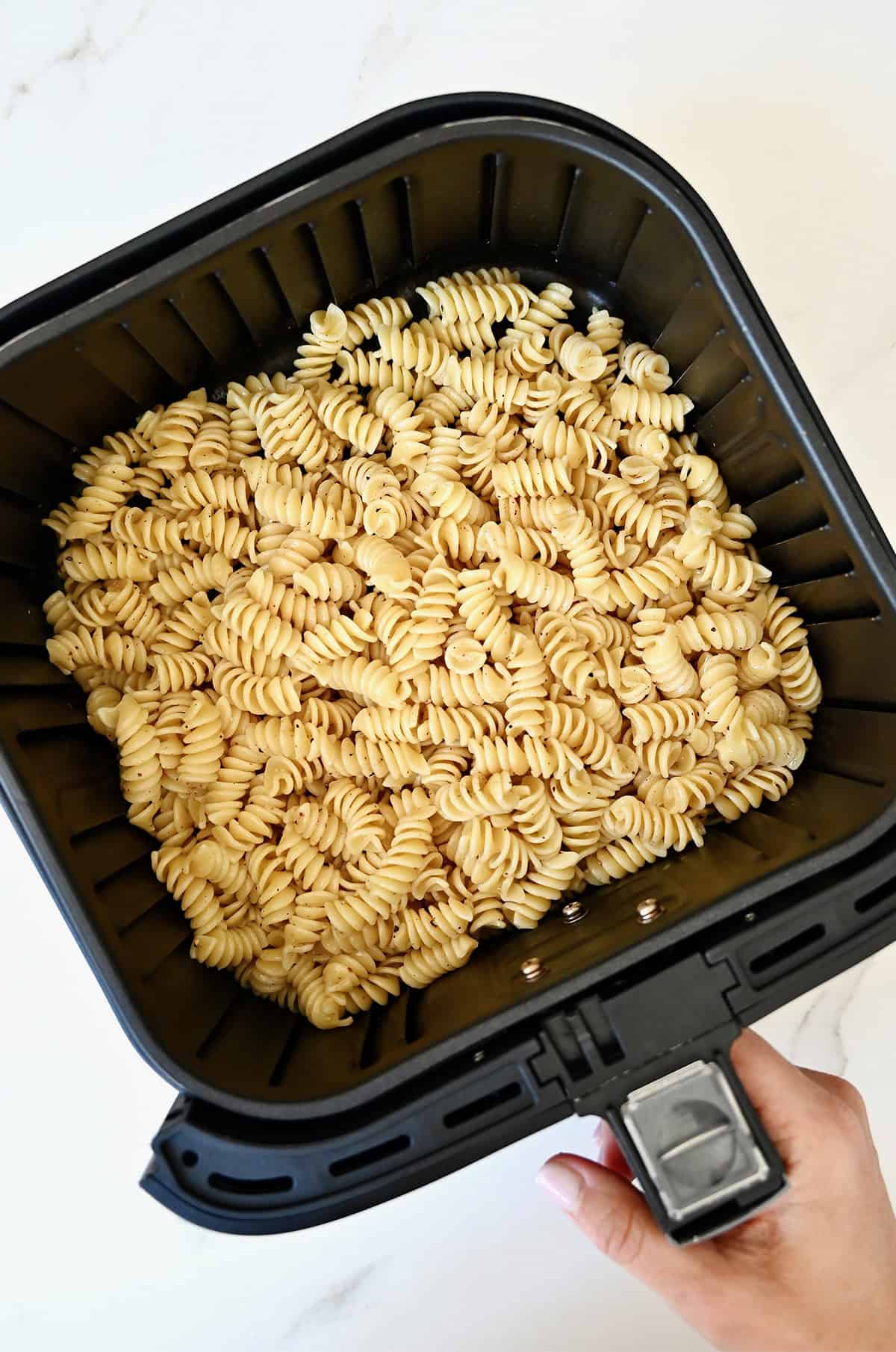 Cooked, olive oil-coated pasta in an air fryer basket.