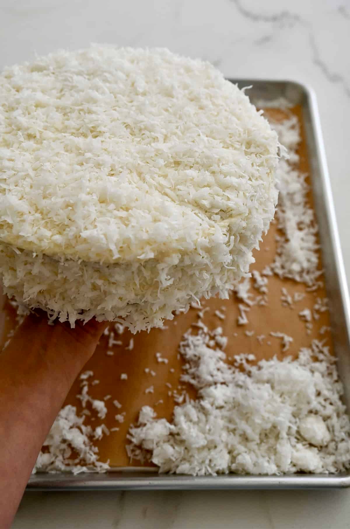 Pressing sweetened flaked coconut onto a cream cheese frosted coconut layer cake.