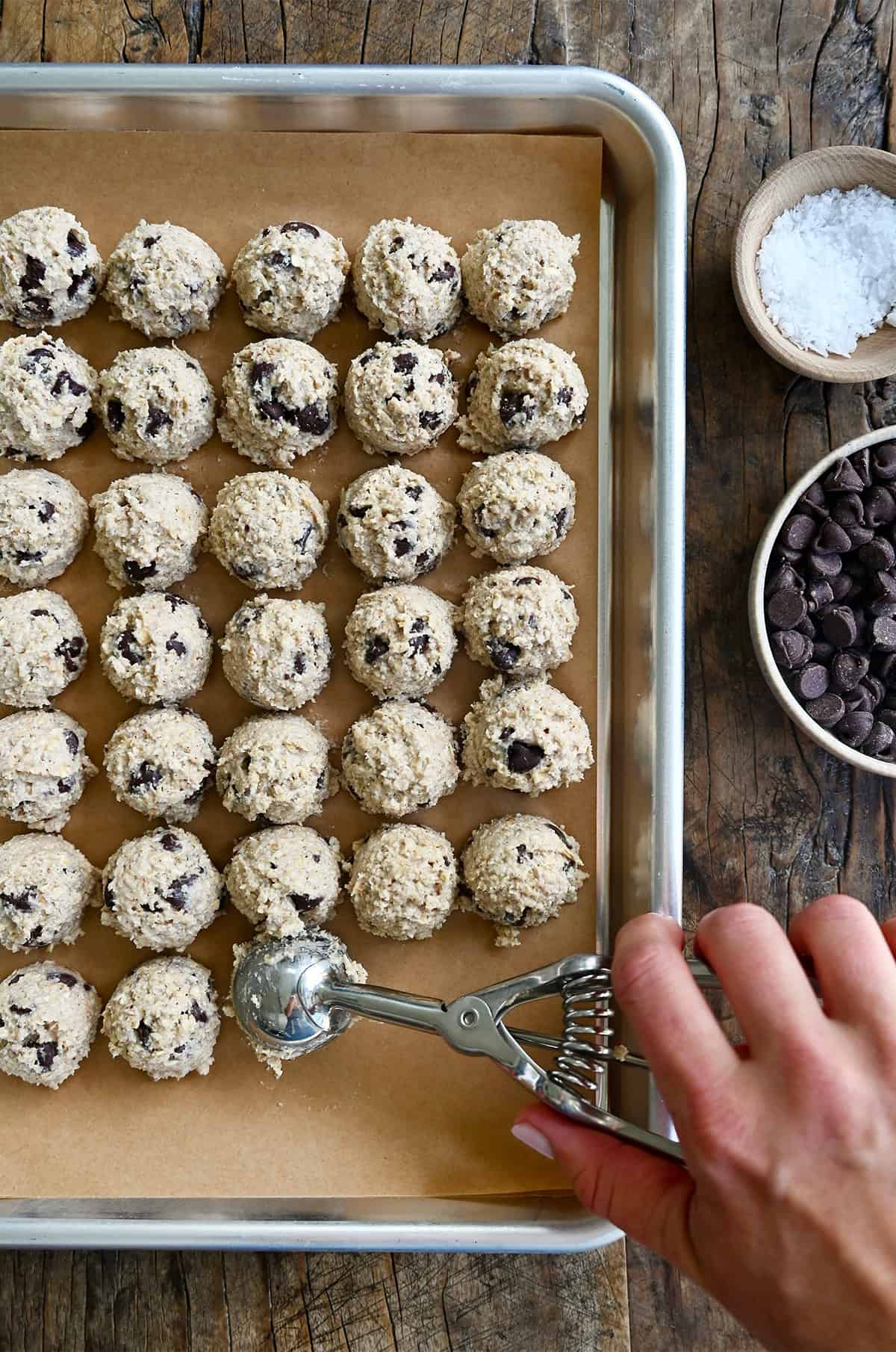 Scooping balls of protein-packed cottage cheese cookie dough onto a parchment paper-lined baking sheet.