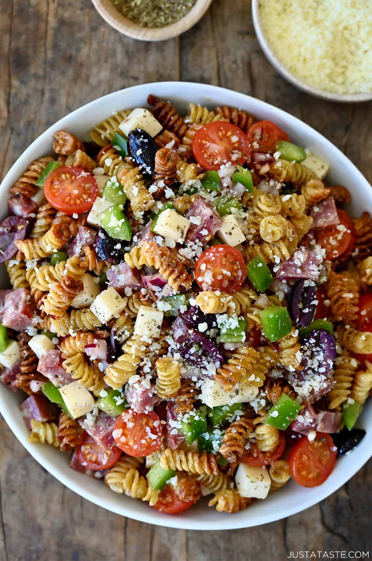 A large white serving bowl of crispy pasta salad made with air-fried rotini, cherry tomatoes, green pepper, salami, provolone, black olives and grated Parmesan.