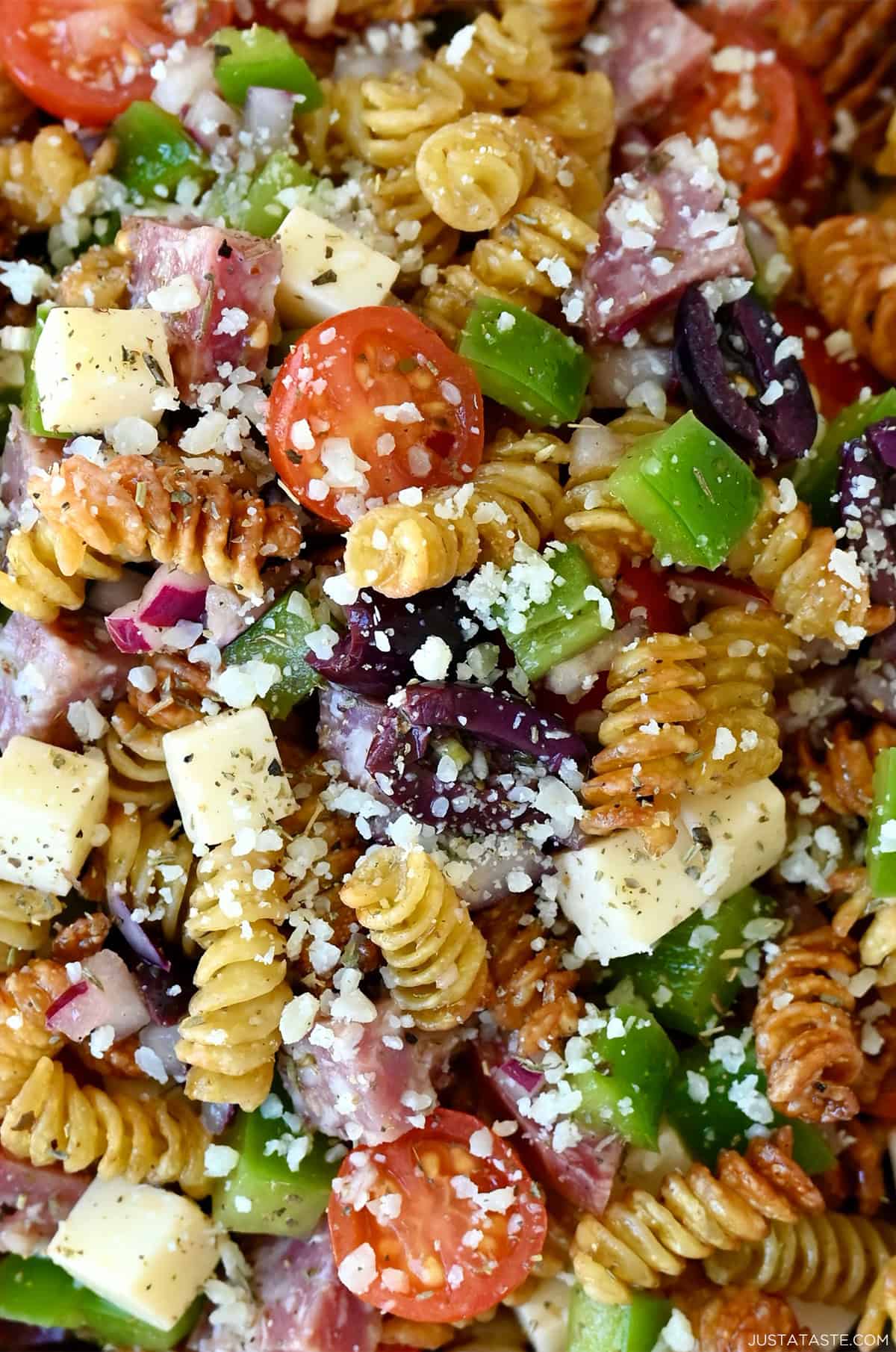 A close-up of crispy pasta salad with crispy air-fried noodles, cherry tomatoes, olives, diced green peppers, cubed provolone cheese, and cubed hard salami, all tossed in Italian dressing and garnished with grated Parmesan.