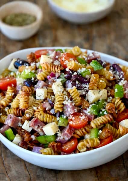 Crispy pasta salad with cubed provolone, salami, olives, tomatoes and diced bell peppers in a large bowl.