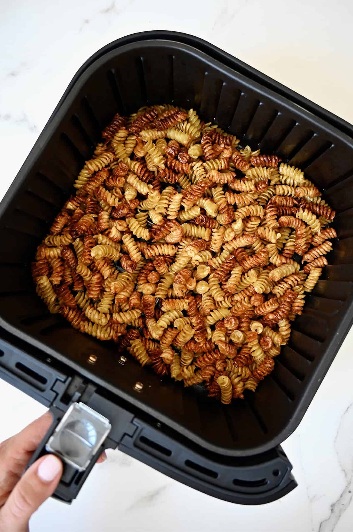 Crispy pasta in the basket of an air fryer.