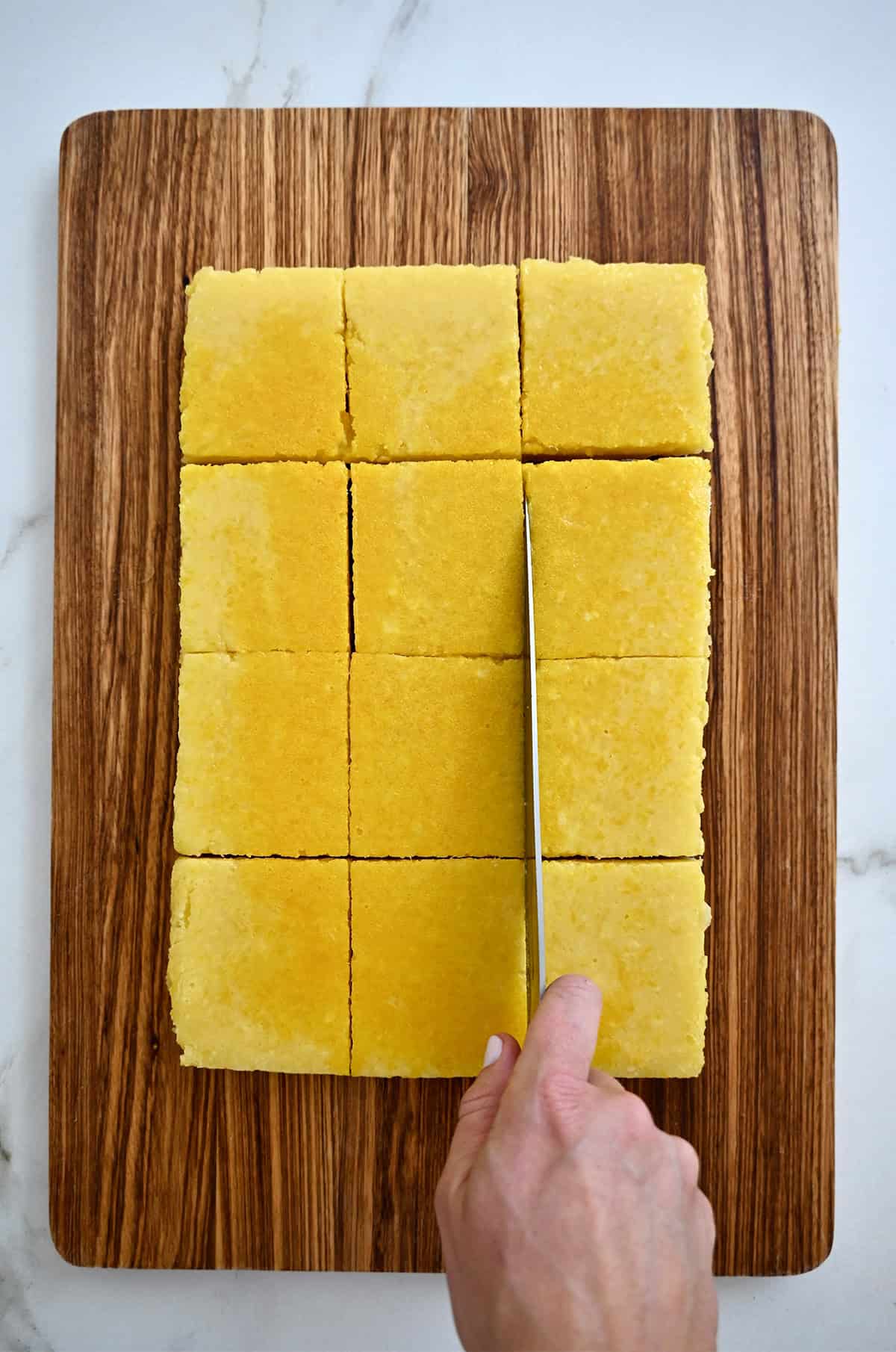 Cutting lemon bars with a sharp knife on a wooden cutting board.