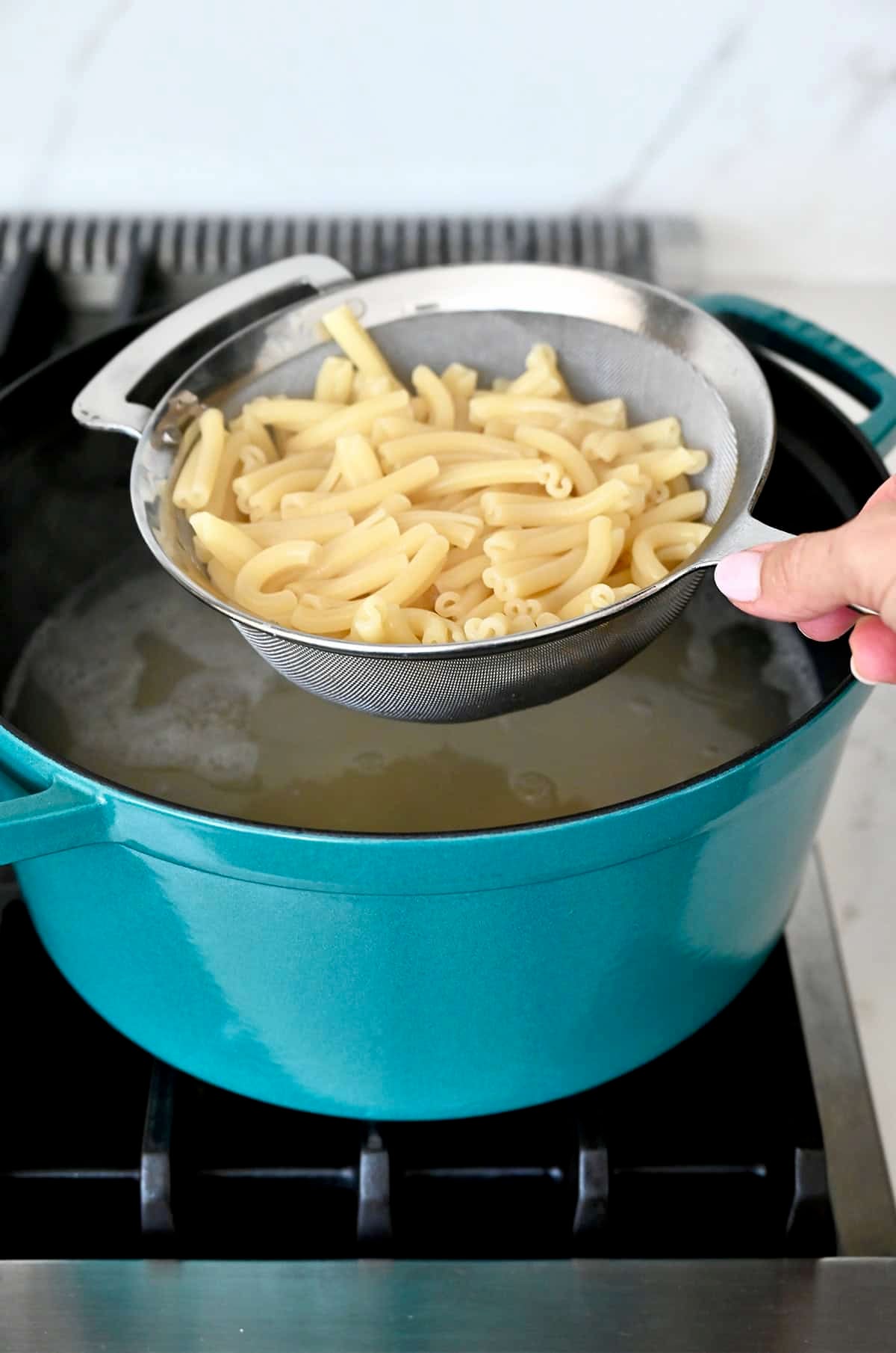 Drain cooked pasta in a sieve over a large pot of boiling water.