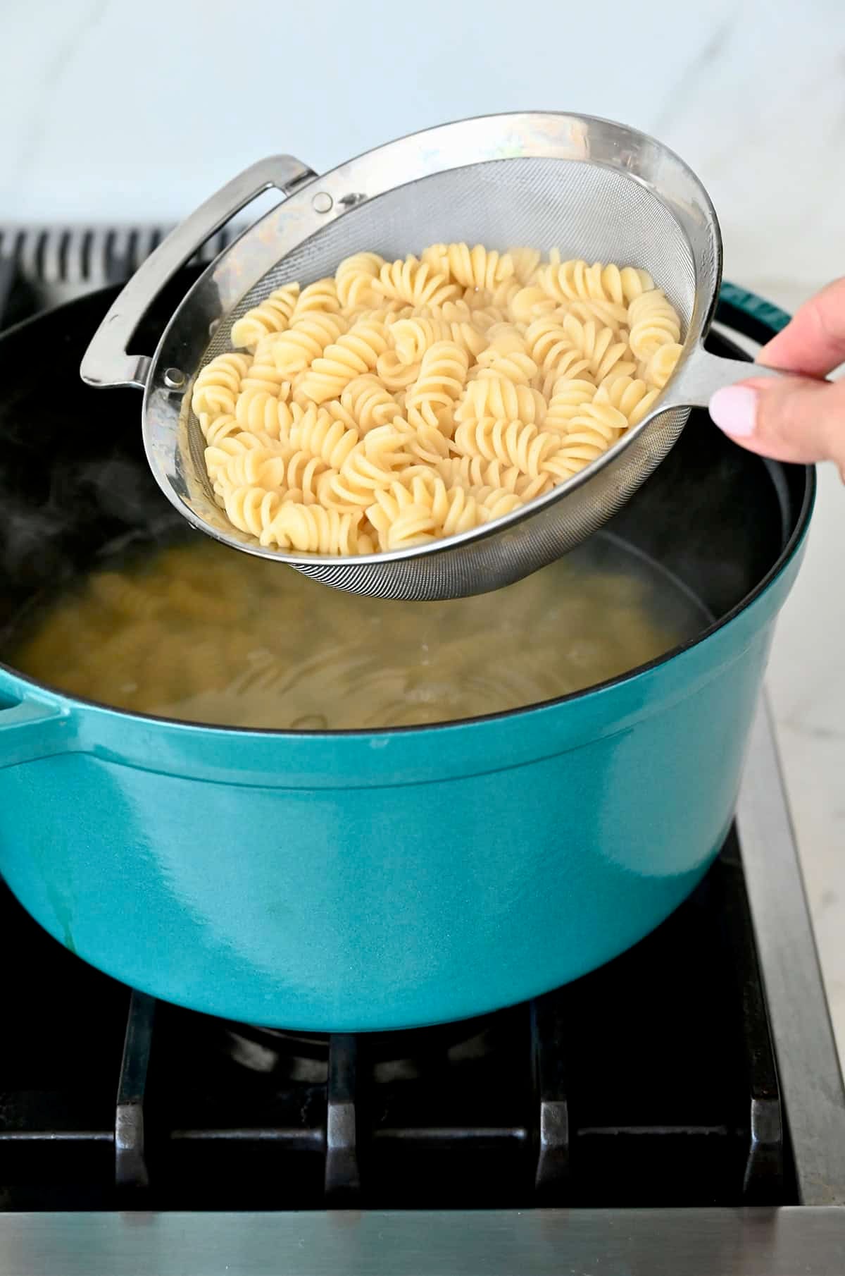 Draining cooked rotini pasta.