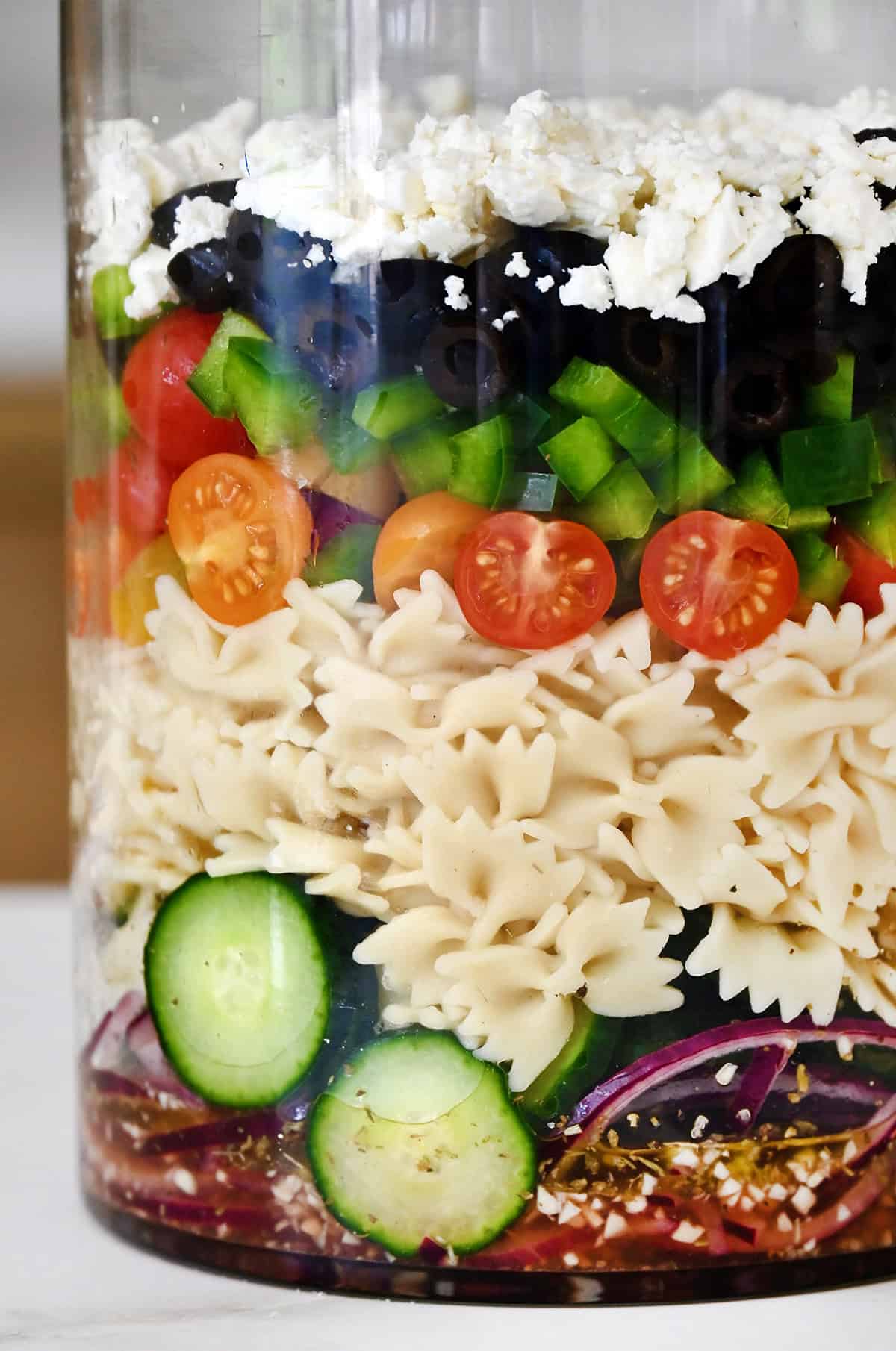 A close-up view of pasta salad layered into a glass container for transporting to a potluck.