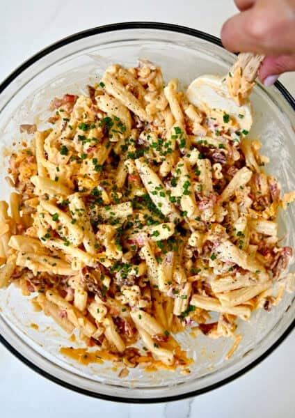 Pimento cheese pasta salad in a big glass bowl with a spatula.