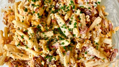 Pimento cheese pasta salad in a big glass bowl with a spatula.