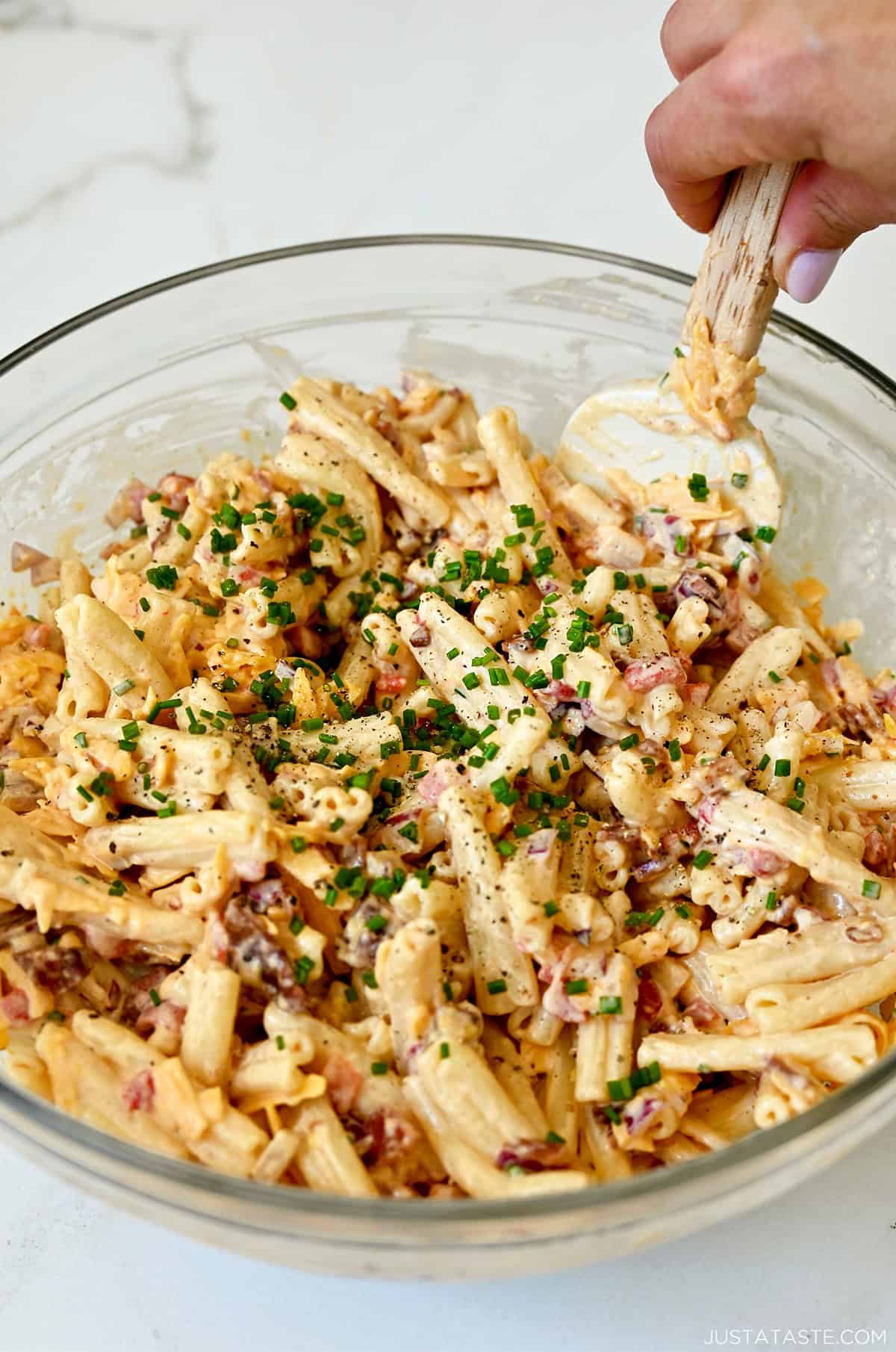 Pimento cheese pasta salad with crumbled bacon and garnished with fresh chives in a large glass bowl.