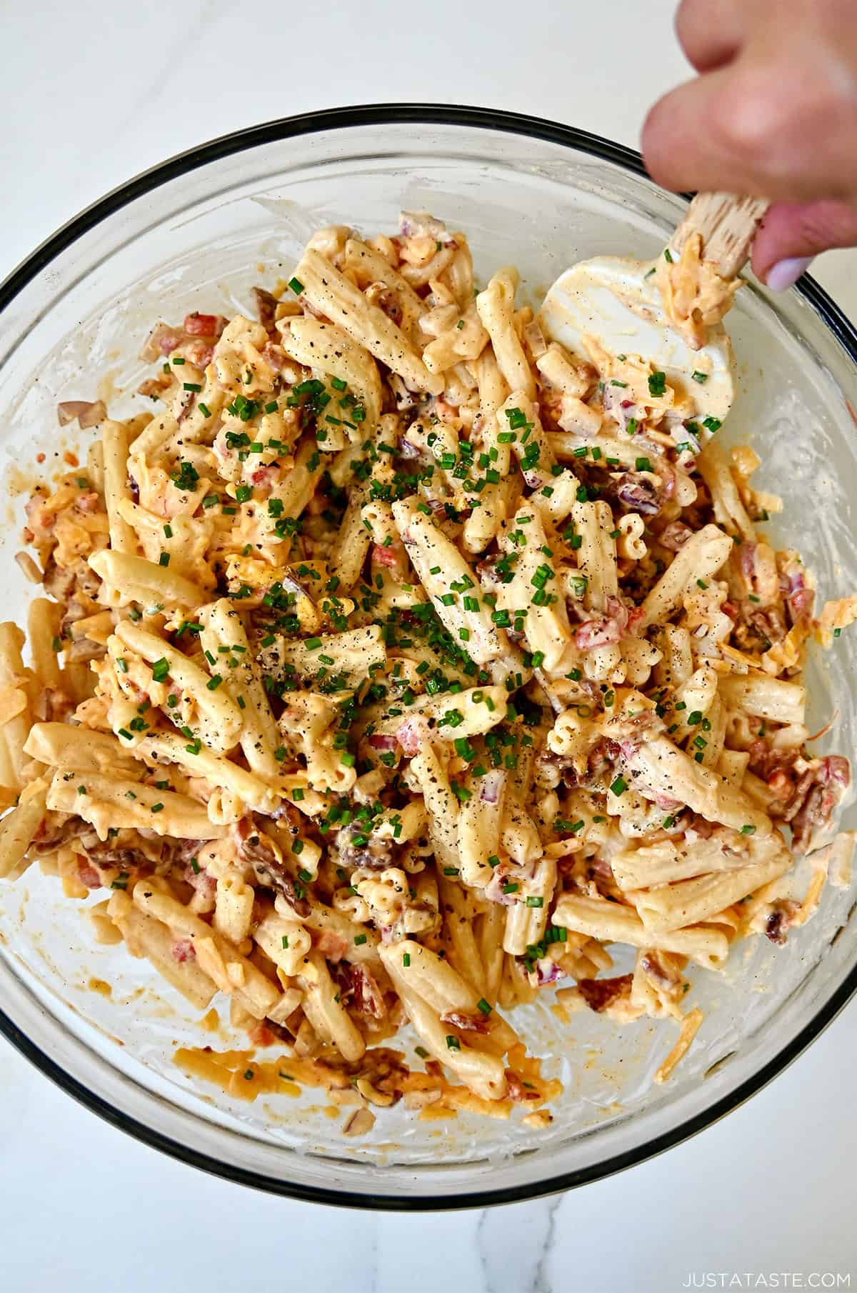 Pimento cheese pasta salad in a big glass bowl with a spatula.