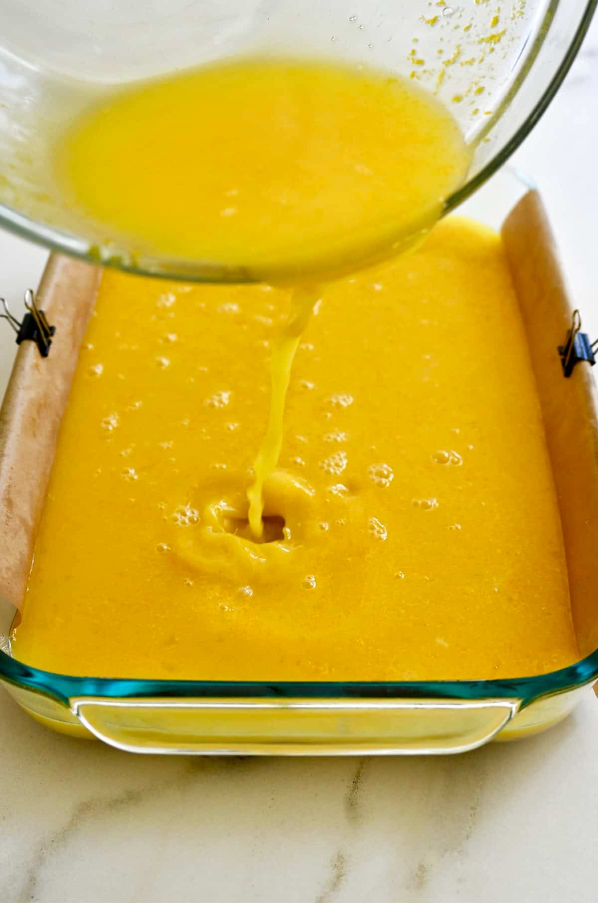 Pouring the lemon filling atop the par-baked shortbread crust in a glass 9x13 baking dish.