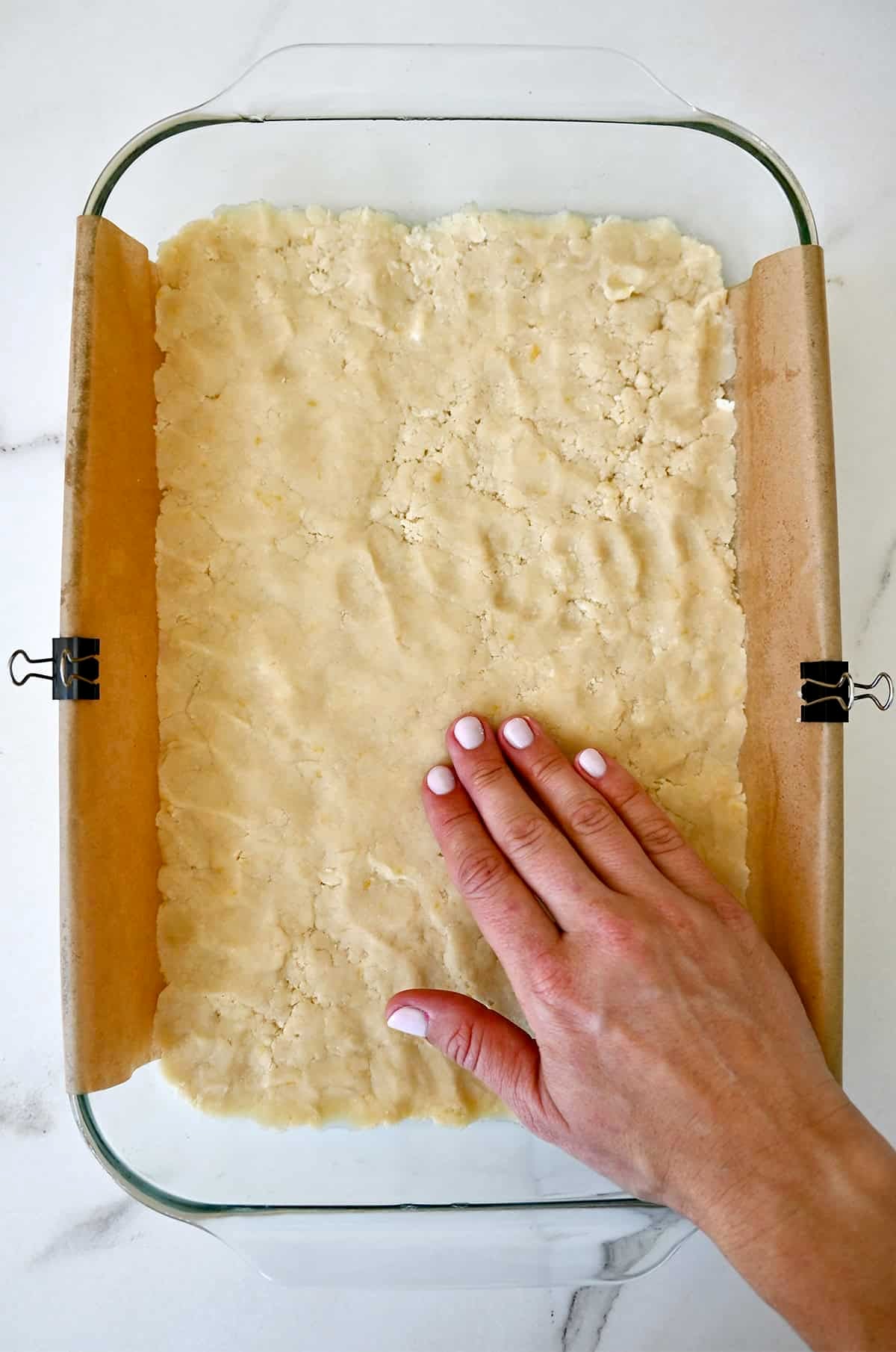 Firmly pressing shortbread dough into a 9x13 baking pan lined with parchment paper secured with all-metal clips.