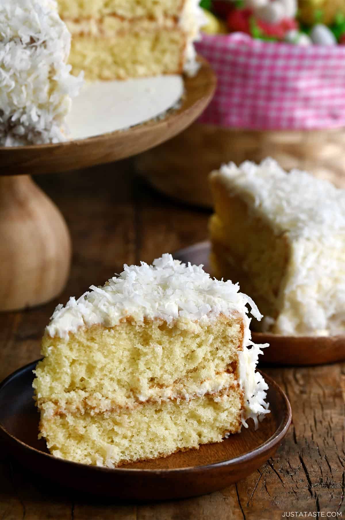 A slice of moist coconut cake with plenty of cream cheese frosting and flaked coconut on a plate.