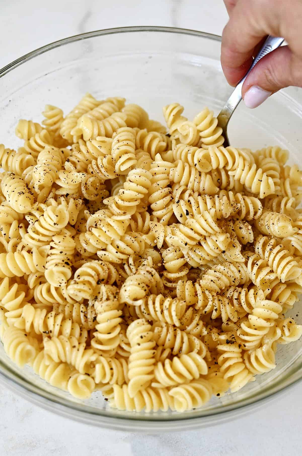 Tossing cooked rotini pasta in olive oil before air frying.