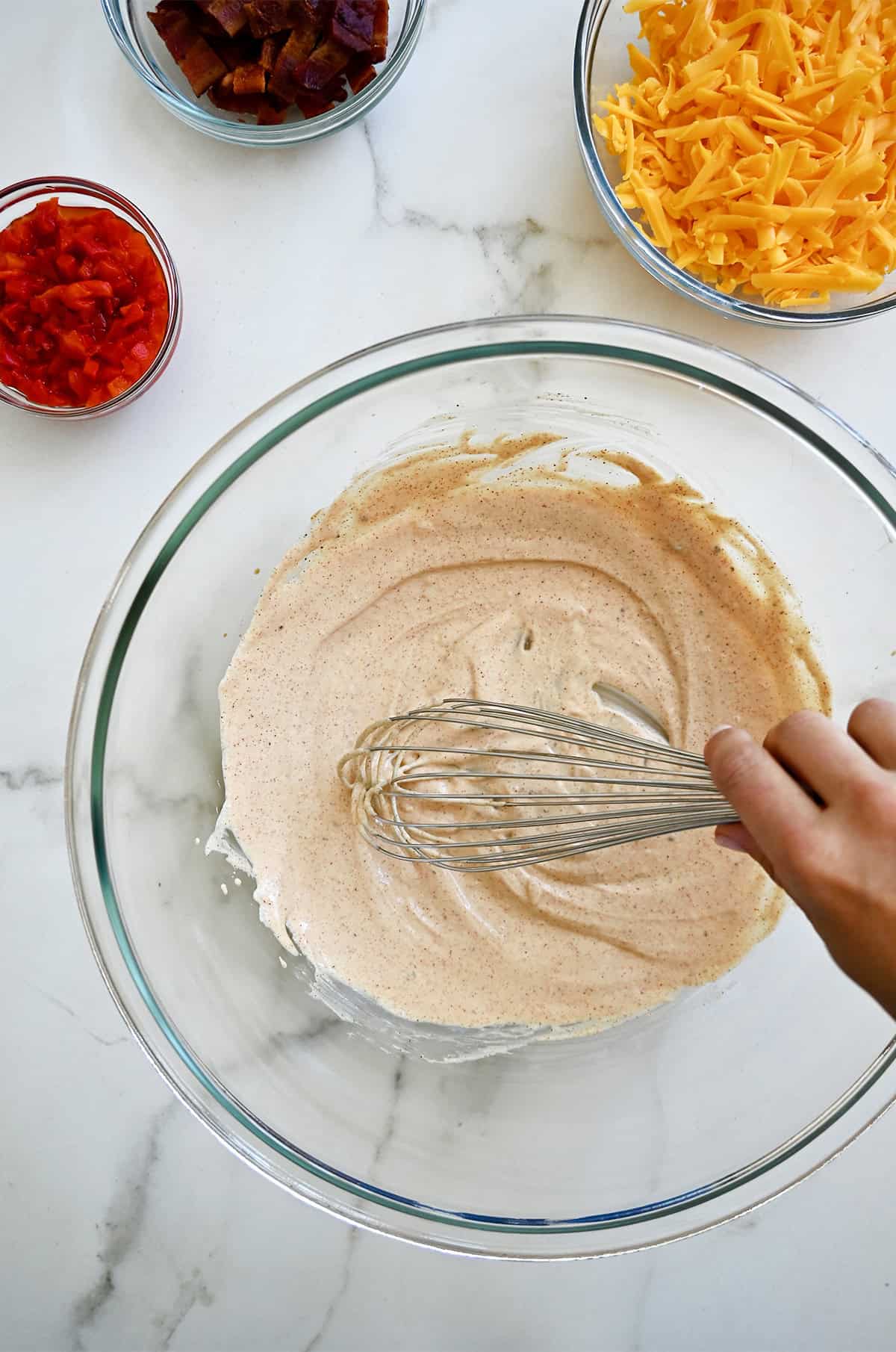 Whisking mayonnaise with paprika and garlic powder in a large bowl.