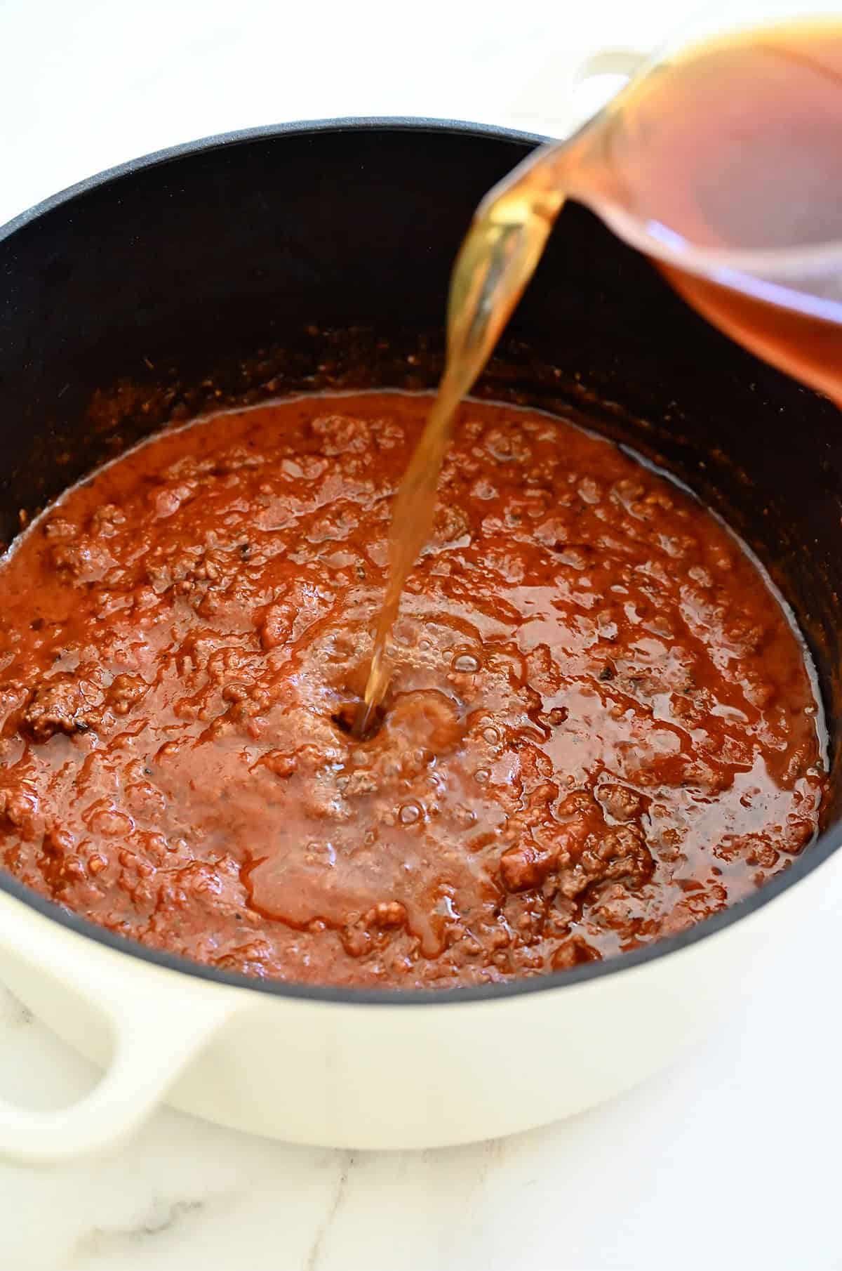 Adding a mixture of beef broth and water to make a bolognese sauce for homemade spaghettiOs.