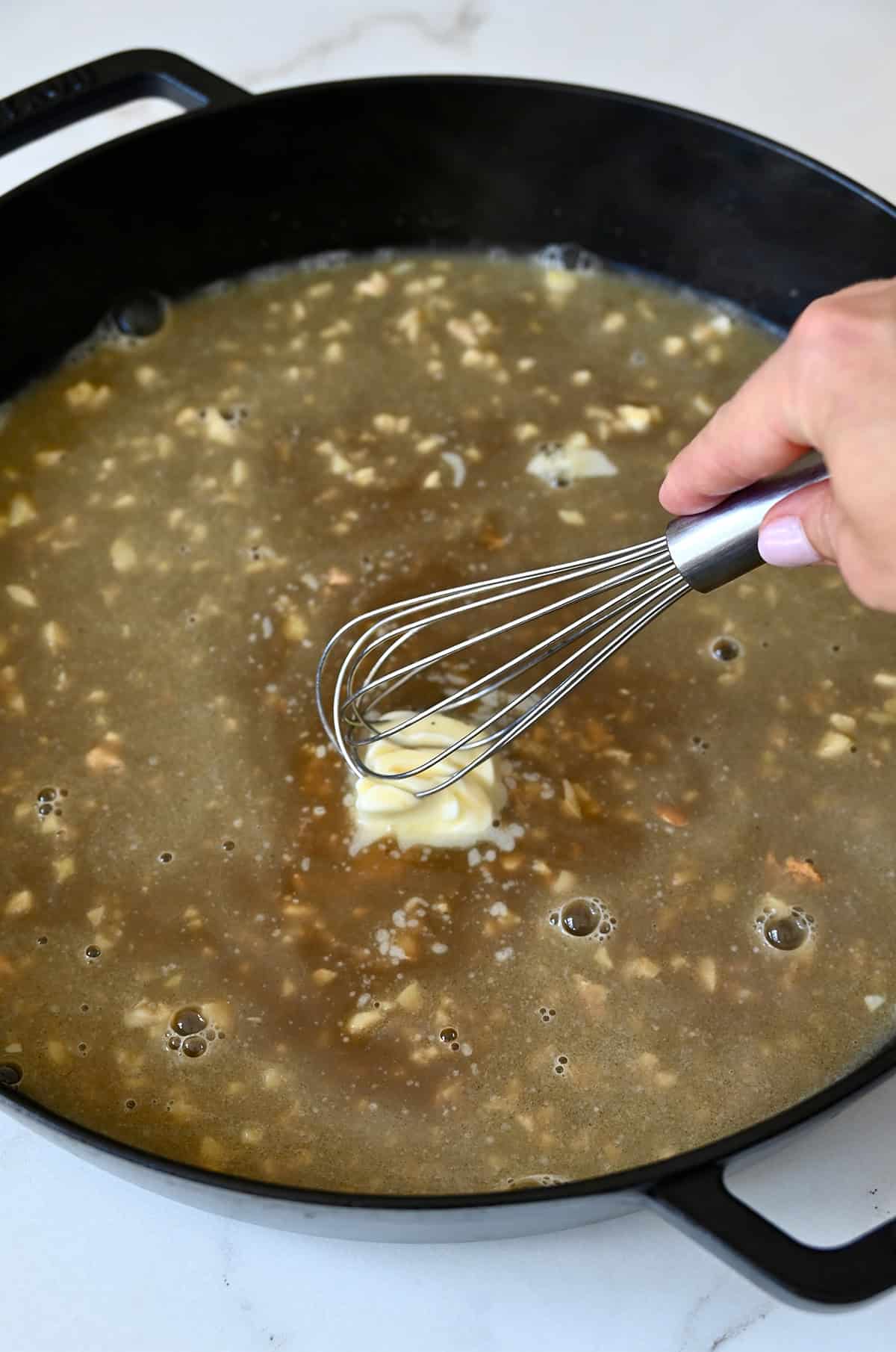Whisking butter into a chicken stock and garlic pan sauce.