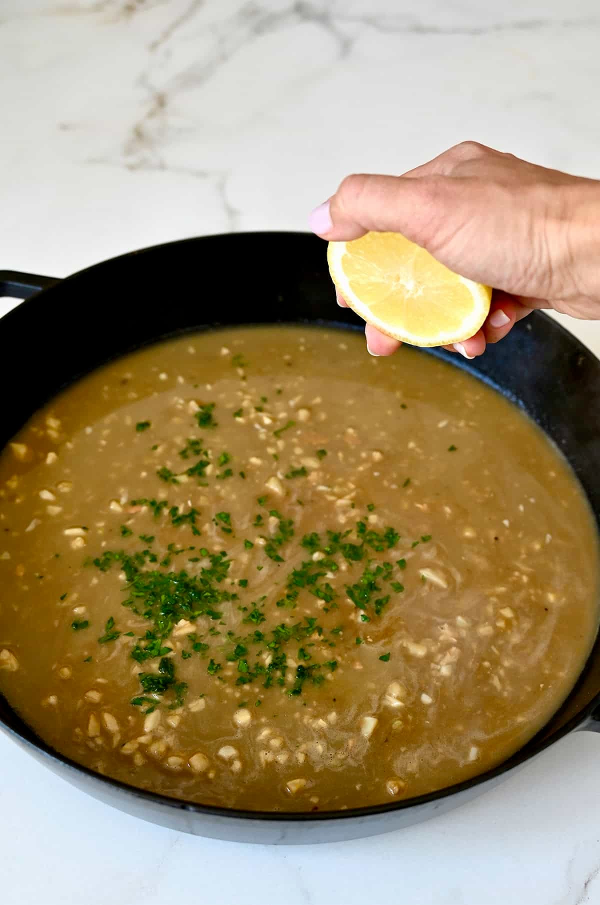 Adding fresh squeezed lemon juice to garlic butter pan sauce with chopped fresh parsley.