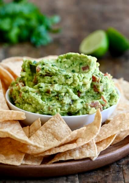 A bowl piled high with homemade guacamole on a serving platter surrounded by tortilla chips.