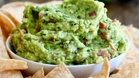 A bowl piled high with homemade guacamole on a serving platter surrounded by tortilla chips.