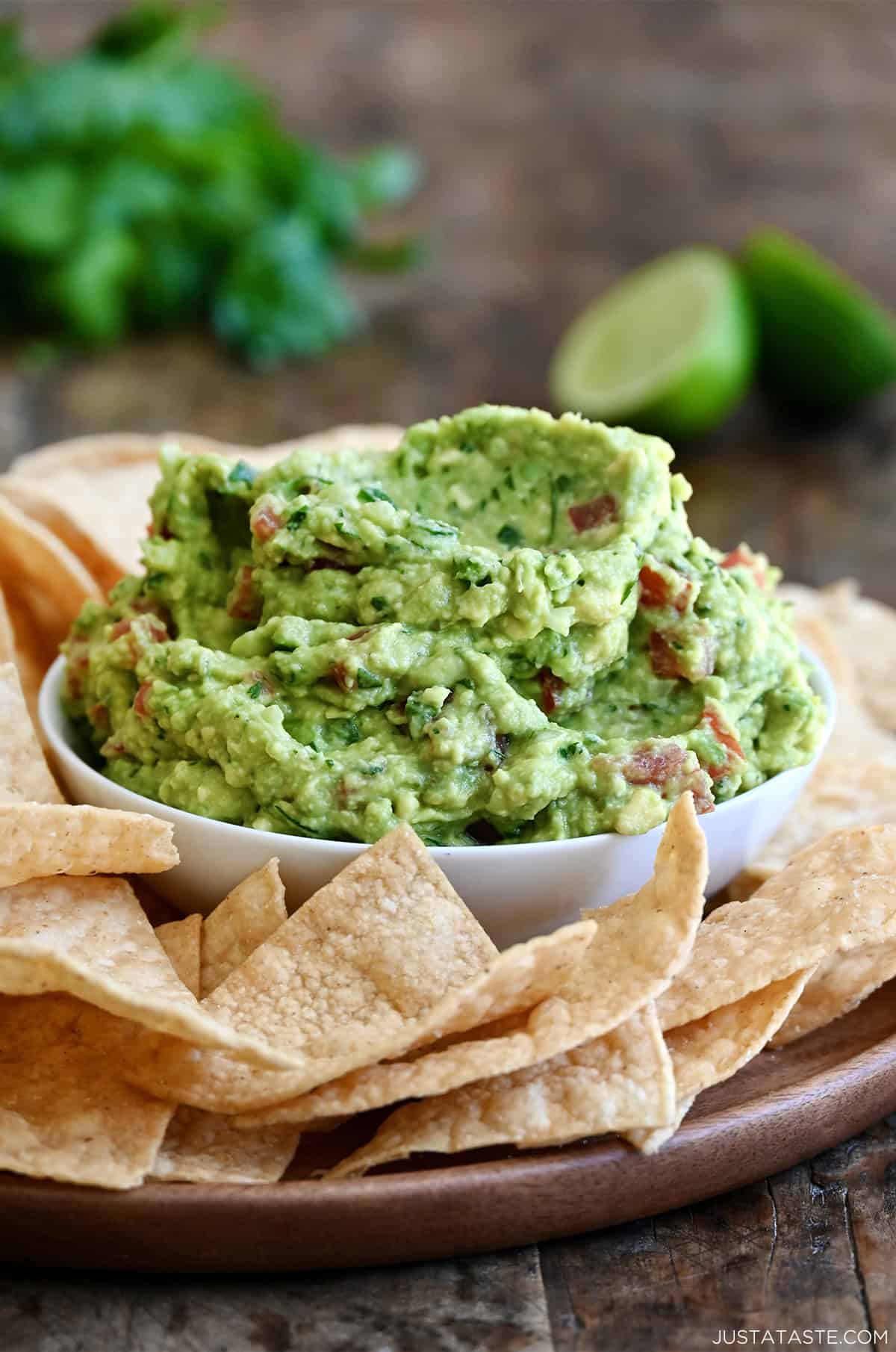 A bowl piled high with homemade guacamole on a serving platter surrounded by tortilla chips.